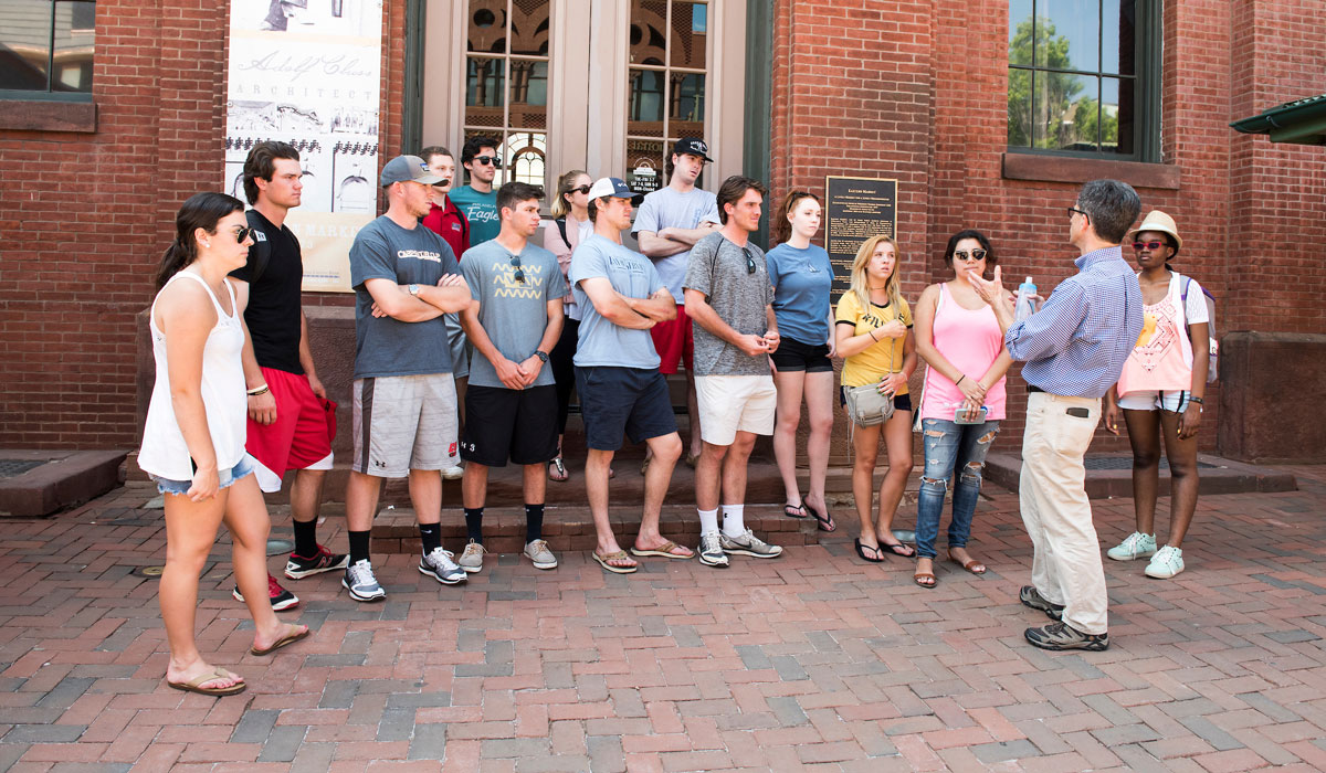 Students listening to professor speak in front of historic building